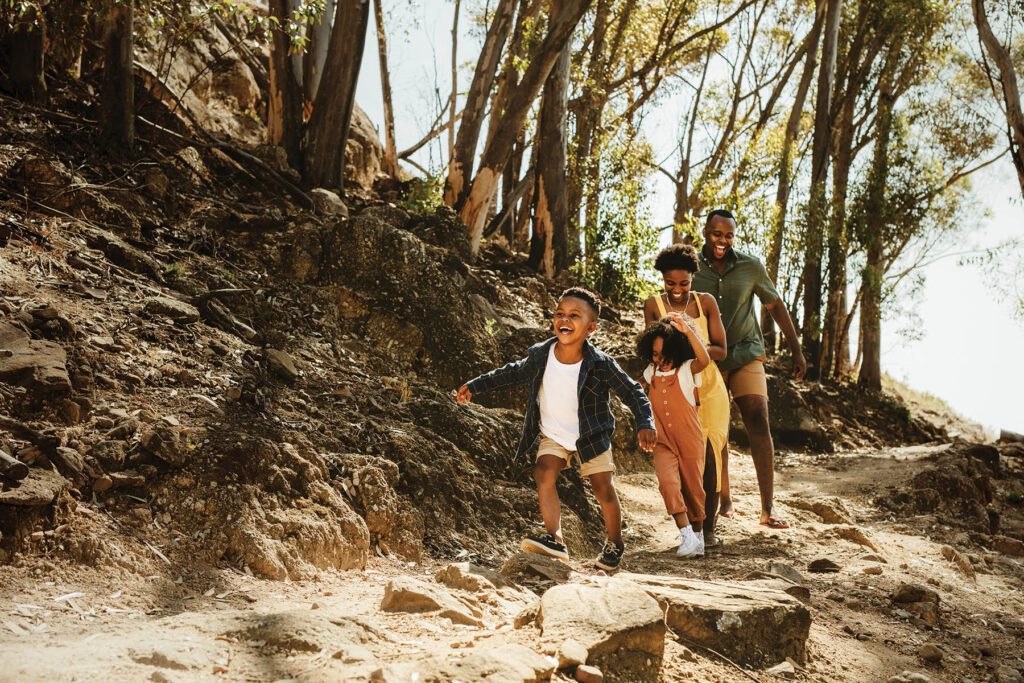 Young family running down rocky mountain trail. Two kids running with parent on a trail in forest.